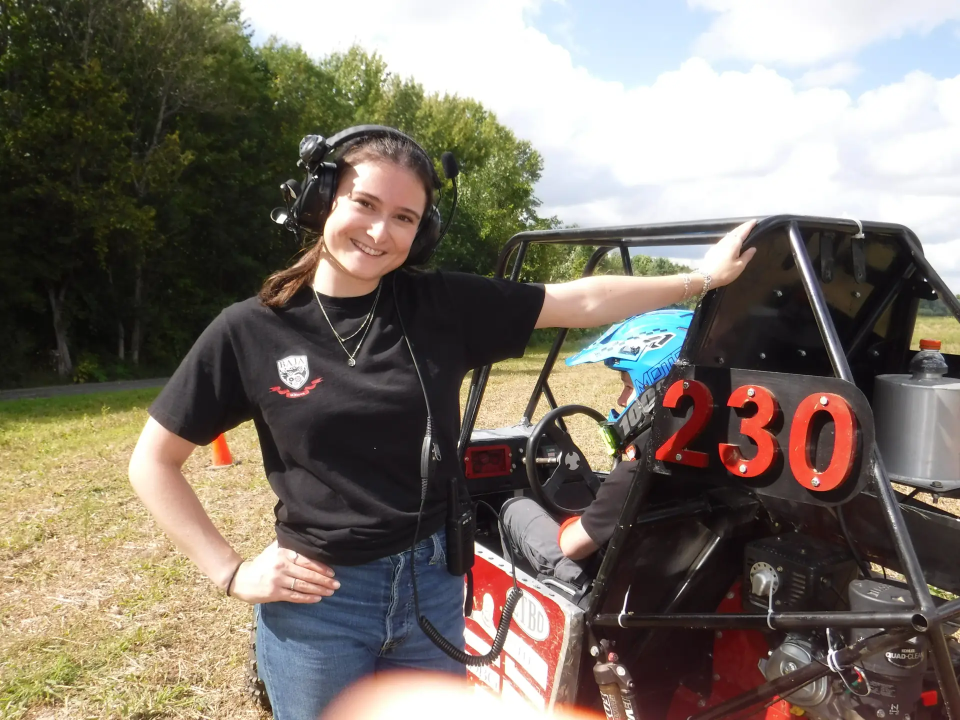 Team member in a team shirt and radio headset beside car #230
