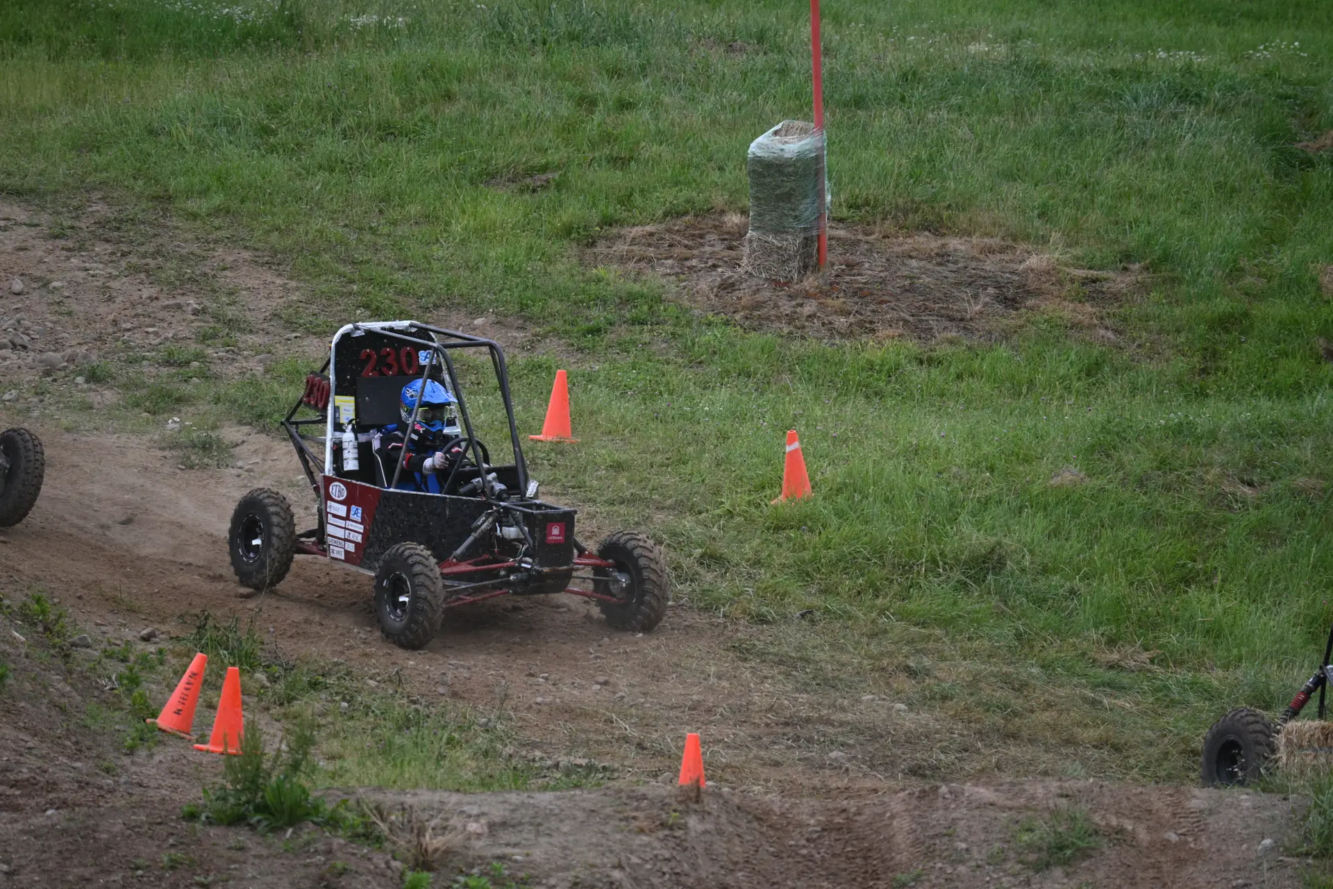 Car #230 driving across a grassy slope between cones