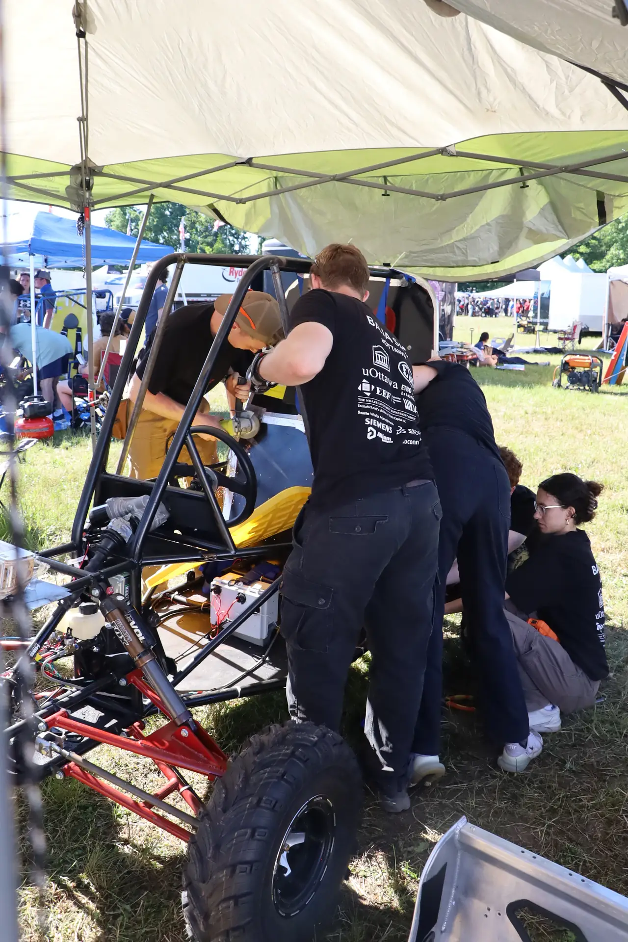 Team members working on the car under the tent