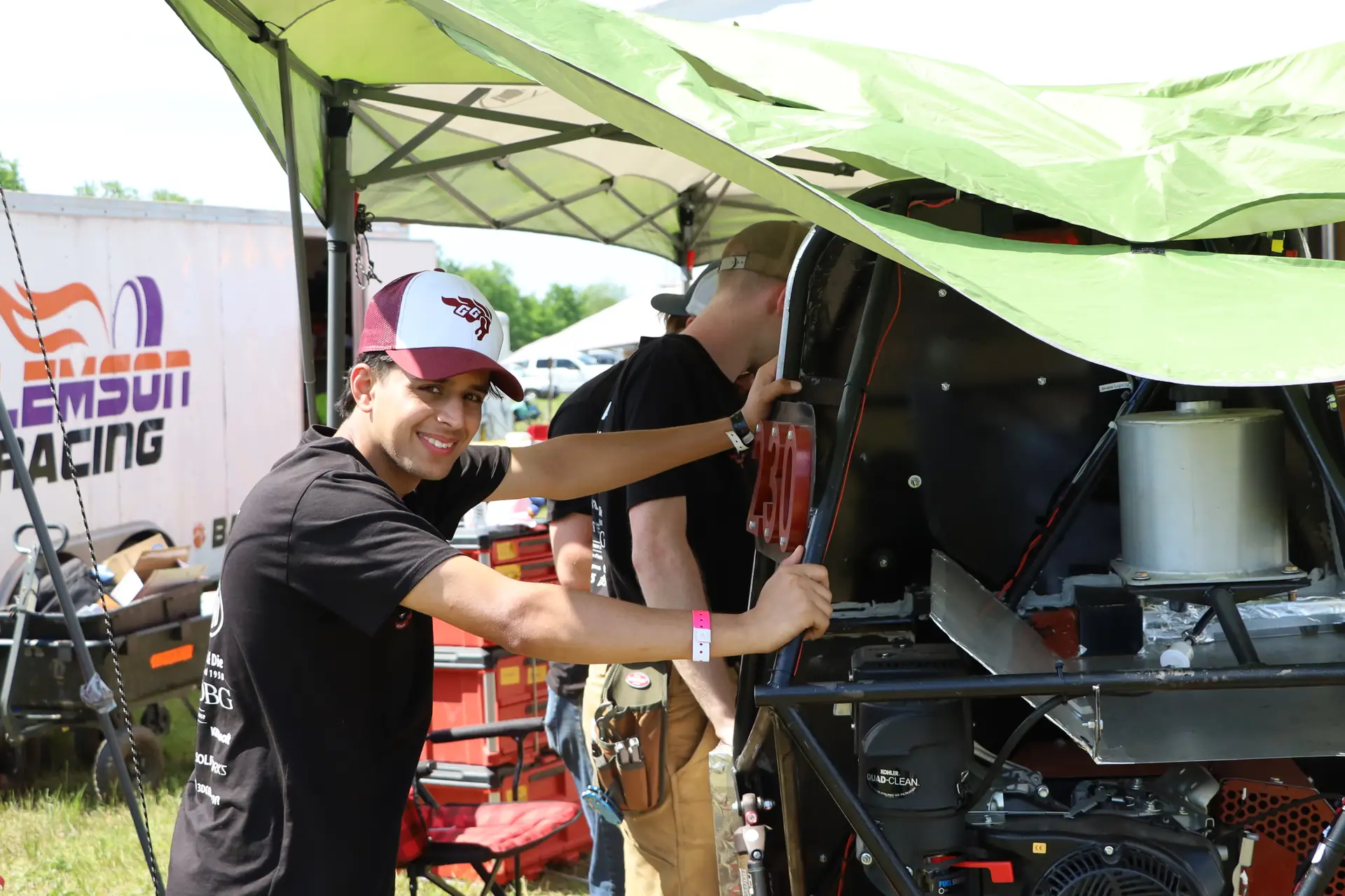 Team member smiling beside the car's engine bay