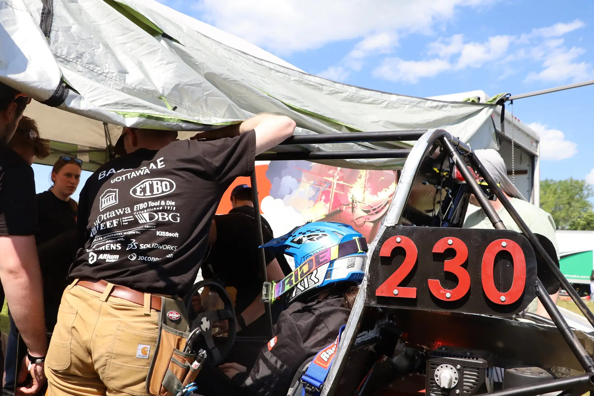 Team members in sponsor shirts working on car #230 under the tent